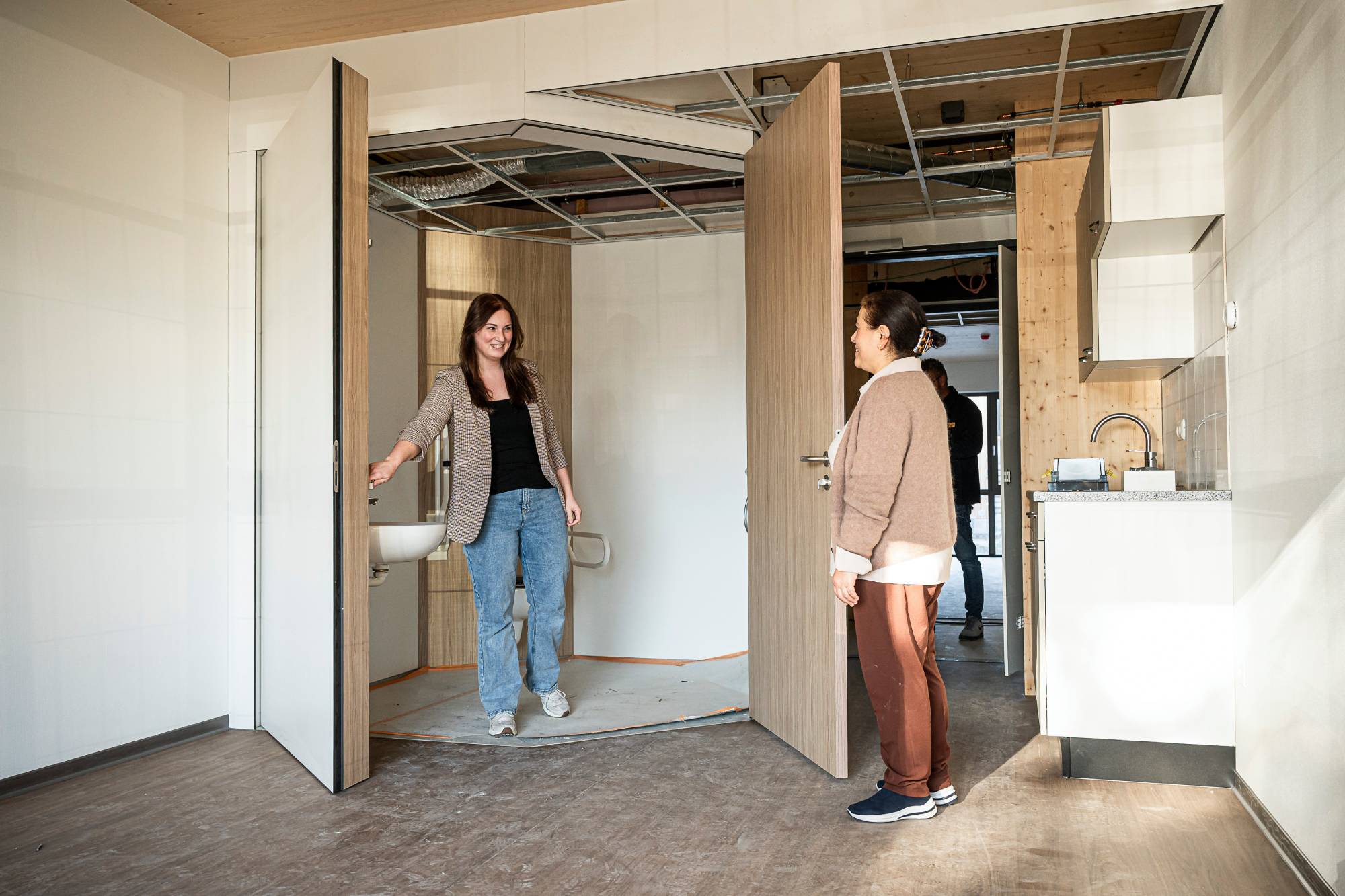 Zorgondernemers Tülay Arslan en Chelsea Verheijen-Lemmens staan in een zorgstudio. De deuren van de doucheruimte draaien open.