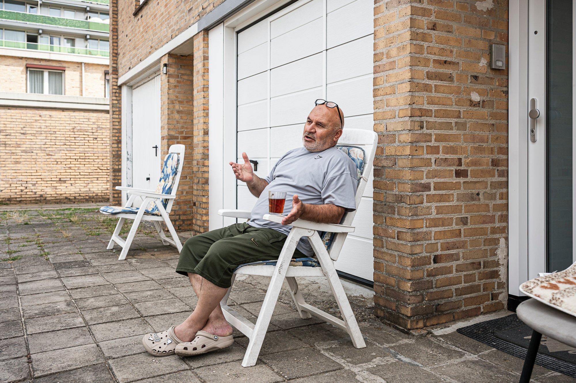 Erdem zit op stoel voor zijn woning. Op de leuning van zijn stoel staat een kopje thee. Op de achtergrond staat een lege stoel.